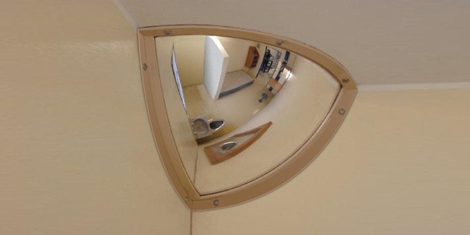 Quarter dome polycarbonate mirror with a surrounding frame installed at a wall and ceiling corner